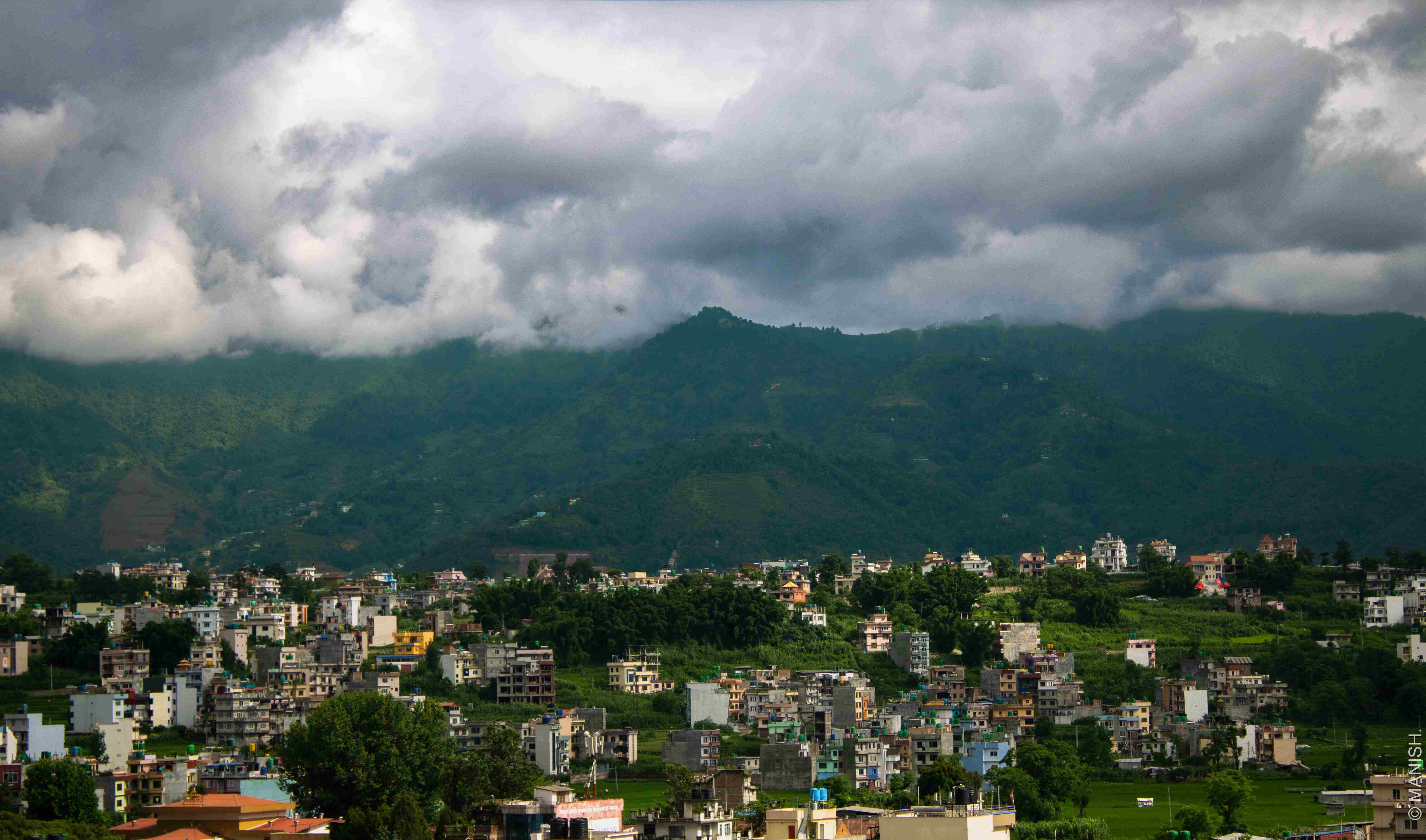 A view from the peak of Bhaktapur, Nepal—where vibrant rooftops meet rolling hills beneath drifting monsoon clouds.